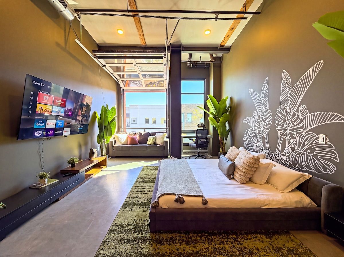 A modern bedroom with a bed, a television mounted on the wall, and a large window.