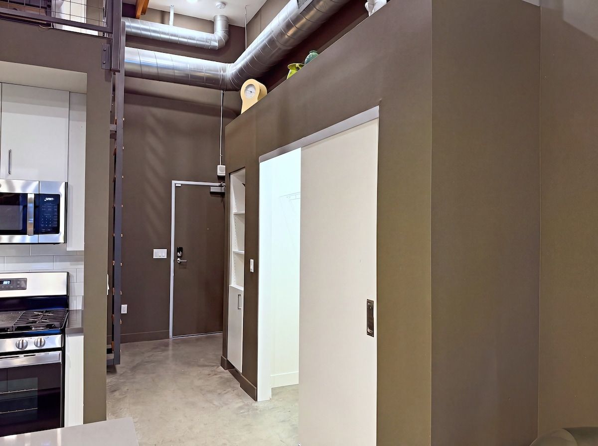 A modern kitchen with stainless steel appliances and a hallway leading to a door.