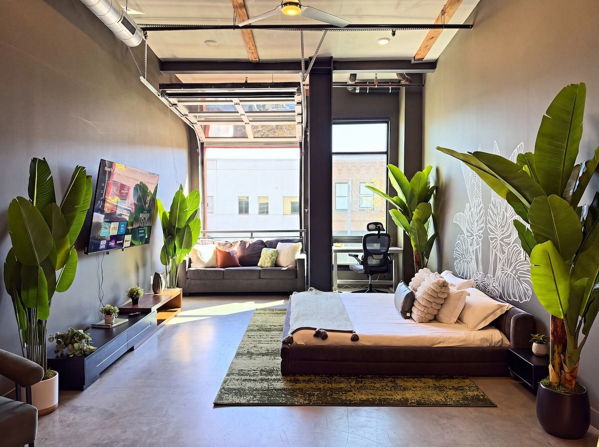 A modern living room with a sofa, a bed, and large potted plants.