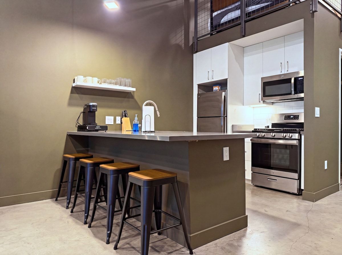 A modern kitchen with a central island, bar stools, a coffee machine, and stainless steel appliances.