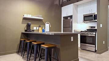 A modern kitchen with a central island, bar stools, a coffee machine, and stainless steel appliances.