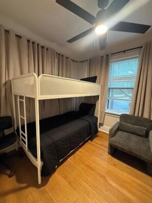 Une chambre avec un lit superposé, un bureau, une chaise, un ventilateur de plafond et une fenêtre avec des rideaux.
