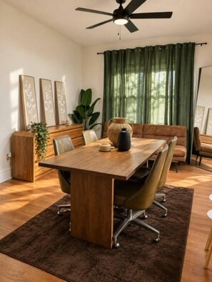 En matplats med ett träbord, stolar, en takfläkt och en grön gardin.
