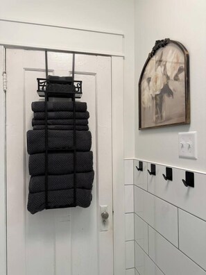 Une porte blanche surmontée d’un porte-serviettes noir où sont pliés des serviettes. Au-dessus du porte-serviettes, on aperçoit une œuvre d’art encadrée.