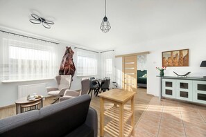 A modern living room with a sofa, dining table, chairs, and a kitchen area with cabinets. - Warsaw | Bukowińska 24A | Comfortable Apartment | Balcony and Parking (Warszawa)