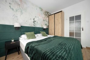 A bedroom with a large bed, a nightstand, a wall-mounted lamp, and a door with frosted glass panels. - Warsaw | Bukowińska 24A | Comfortable Apartment | Balcony and Parking (Warszawa)