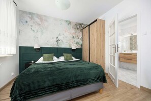 Ein Schlafzimmer mit einem Bett, einem Nachttisch, einer Wand mit floralem Wandbild und einer Holztür zu einem Badezimmer.