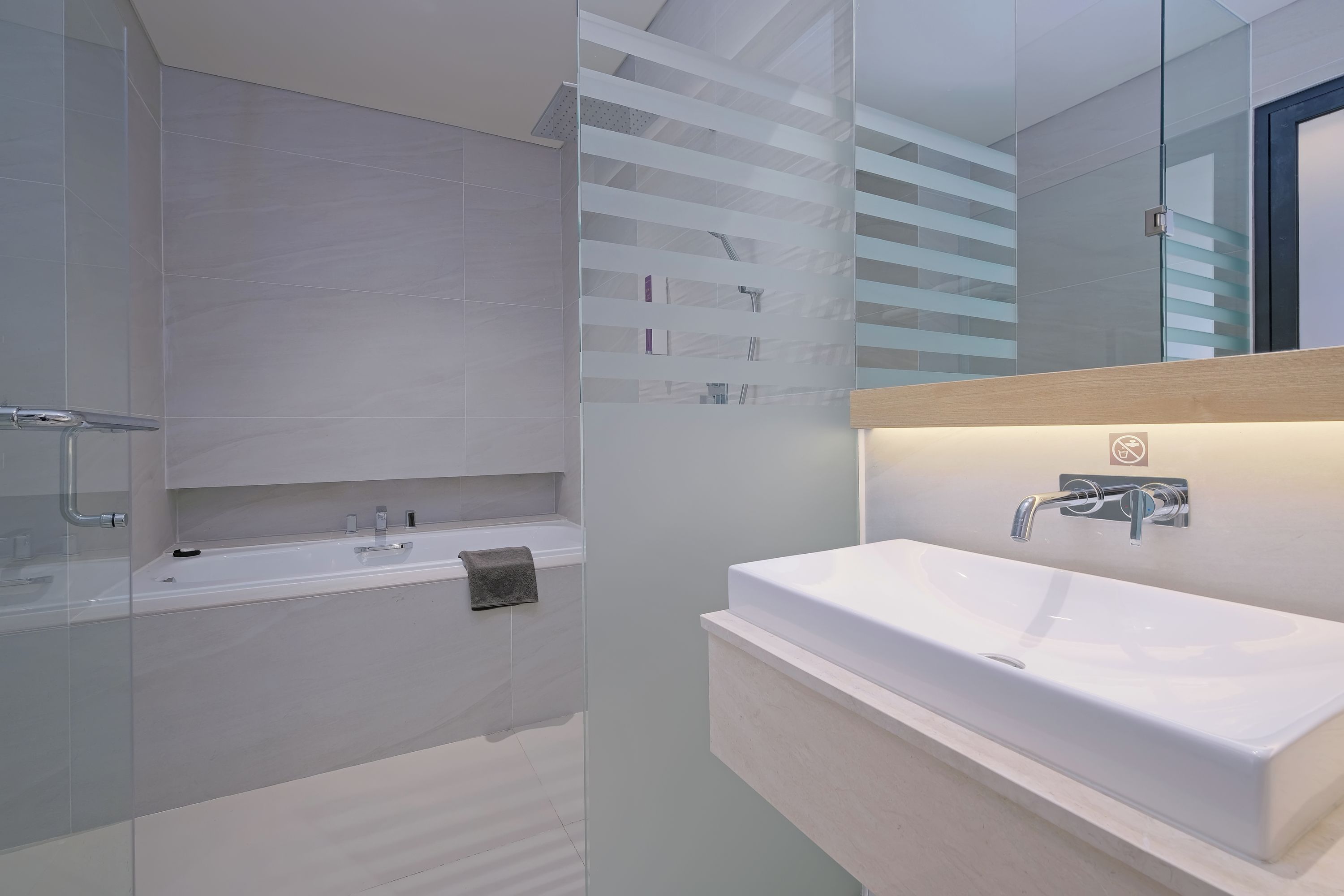 Een moderne badkamer met een grote spiegel, een wit wastafelmeubel en een douchecabine met glazen wanden.