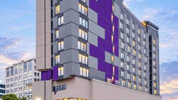 Un hotel moderno con una fachada distintiva en tonos morado y gris, varios balcones y un acceso con techo rojo.