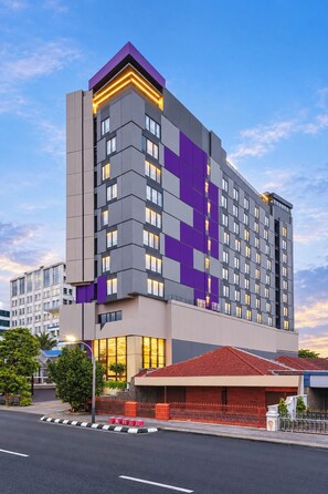 Un hotel moderno con una fachada distintiva en tonos morado y gris, varios balcones y un acceso con techo rojo.