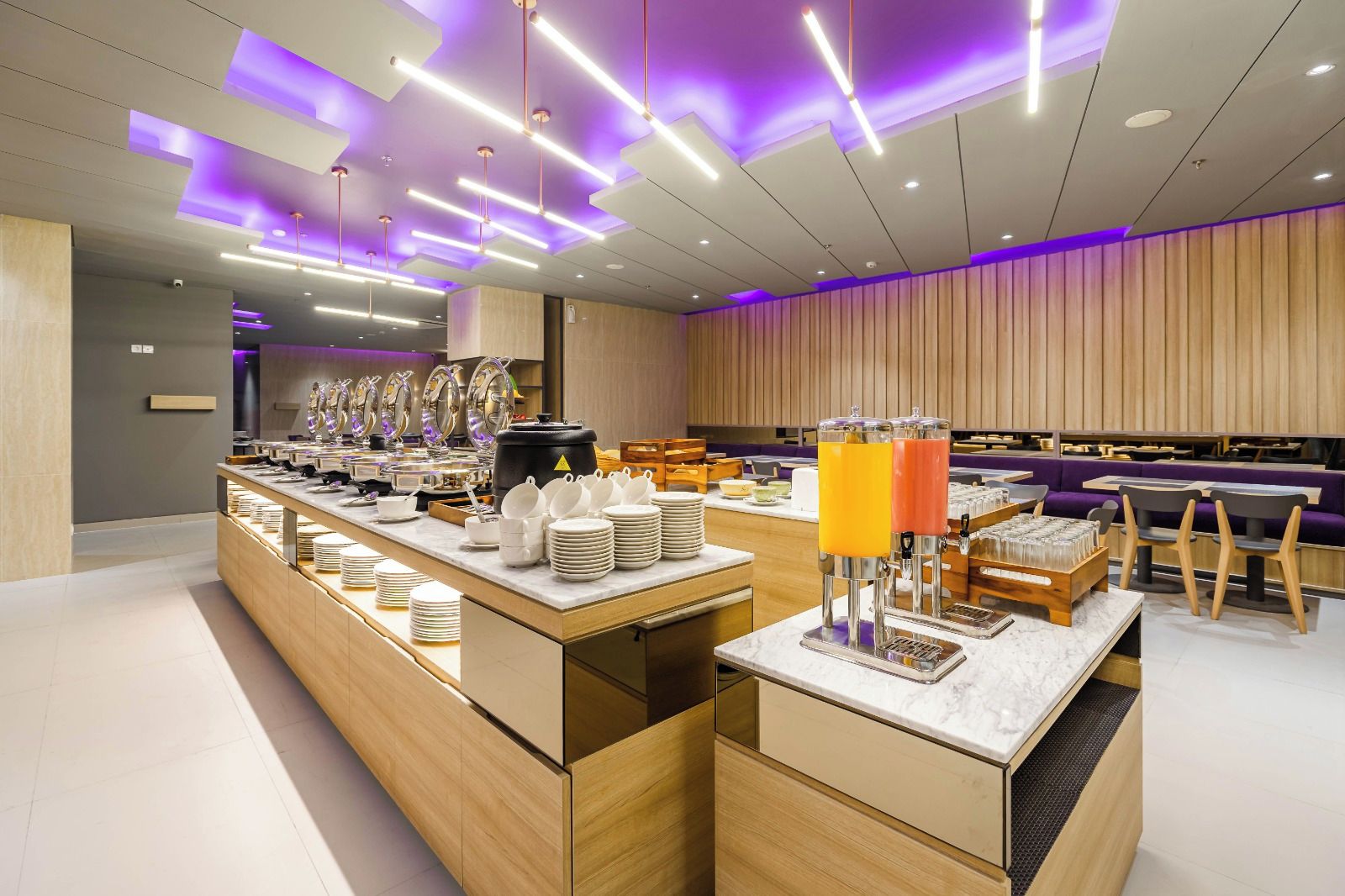 Un moderno comedor para el desayuno con un sistema de buffet variado, que incluye diferentes platos y bebidas, además de una zona de estar con mesas y sillas.