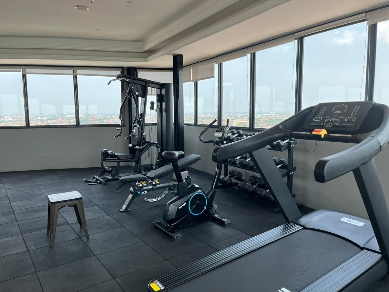 A gym with exercise equipment, a small stool, and large windows offering a city view.