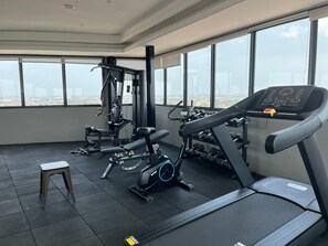 A gym with exercise equipment, a small stool, and large windows offering a city view.