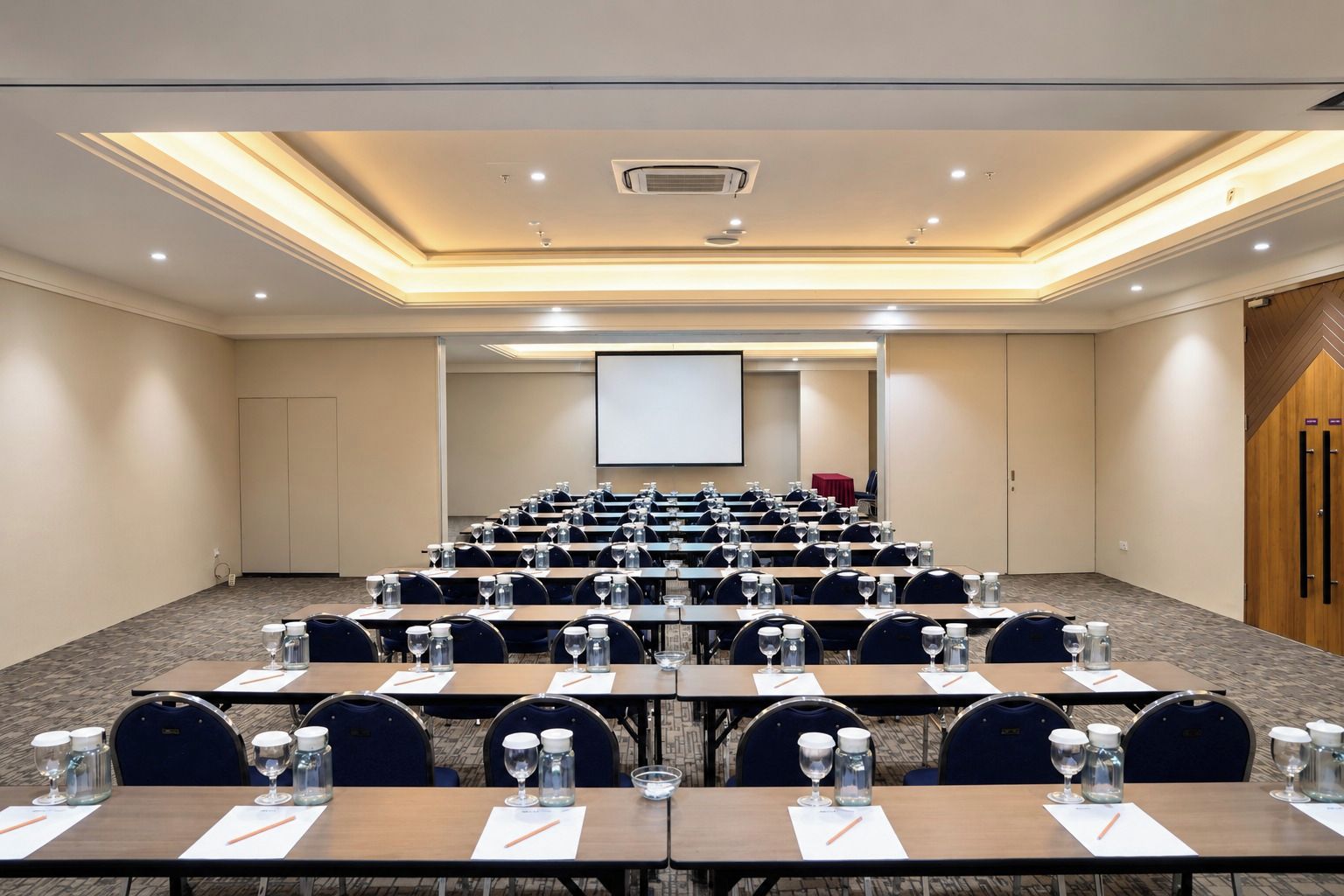 A conference room with rows of tables, chairs, and a projection screen at the front.