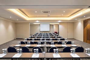 A conference room with rows of tables, chairs, and a projection screen at the front.