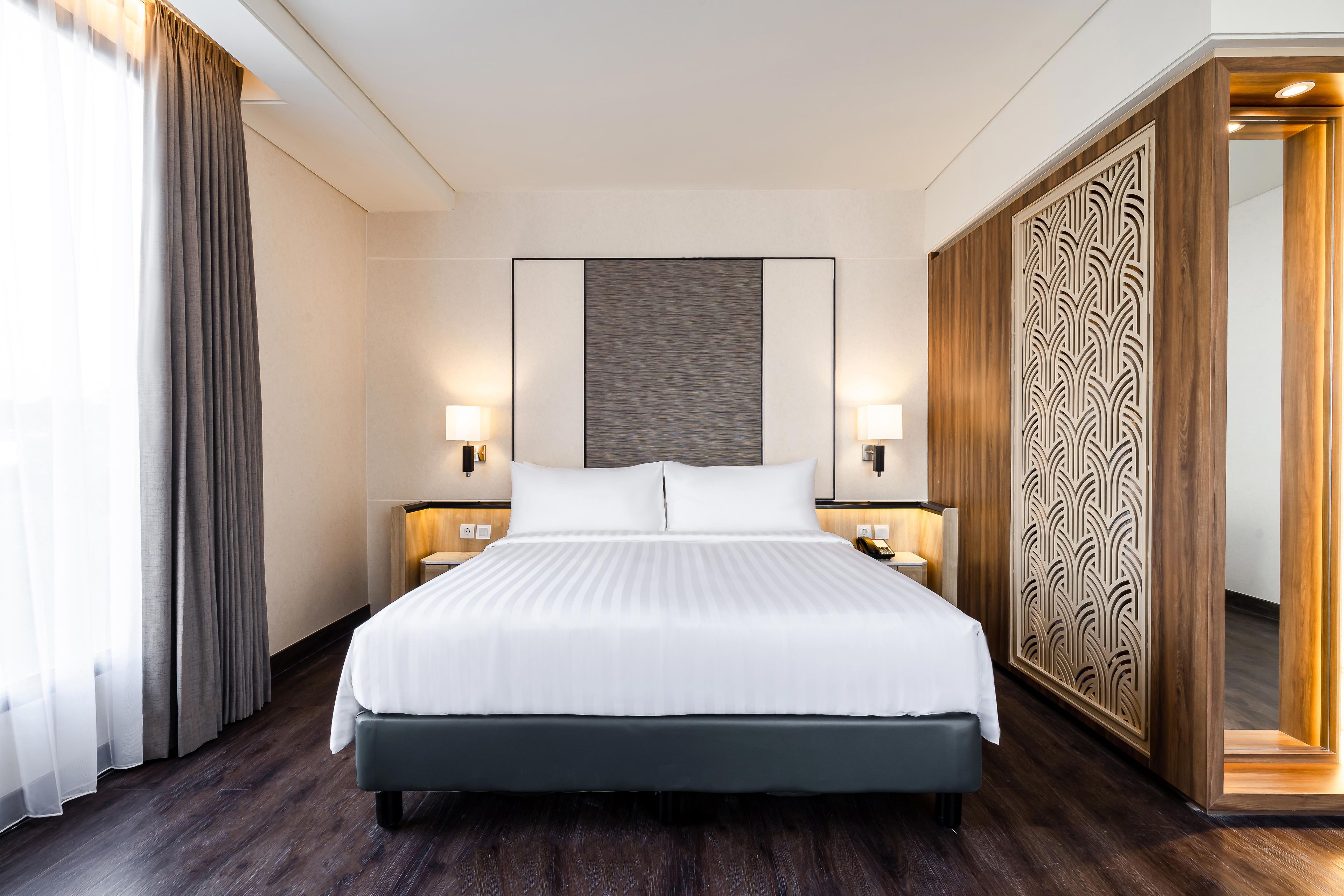 Habitación de hotel con una cama grande, dos mesitas de noche con lámparas, un armario de madera y un espejo amplio.