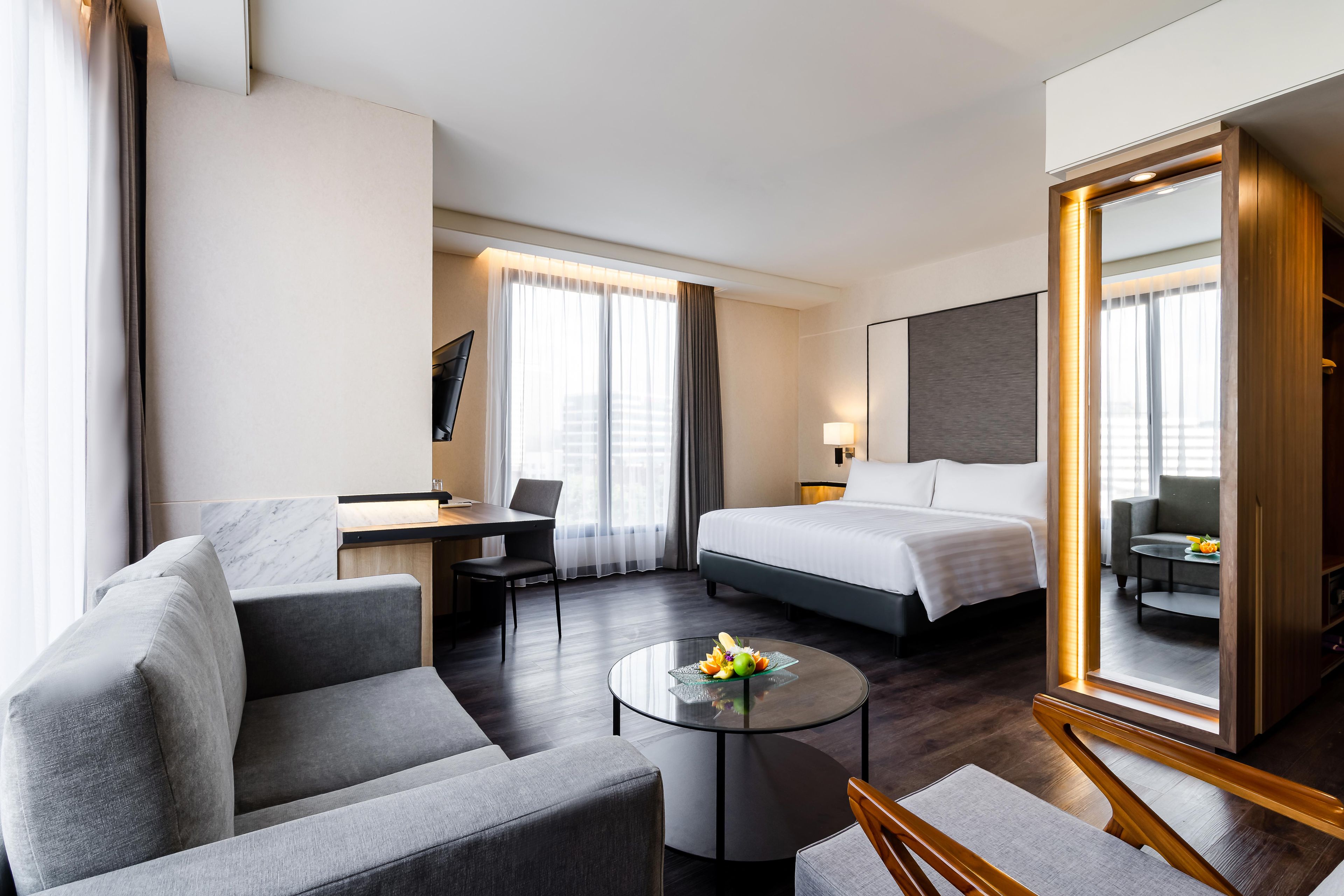 Habitación de hotel con cama, escritorio, silla, sofá y una mesa redonda con fruta.