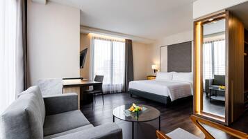 Habitación de hotel con cama, escritorio, silla, sofá y una mesa redonda con fruta.