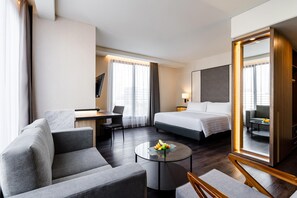 Habitación de hotel con cama, escritorio, silla, sofá y una mesa redonda con fruta.