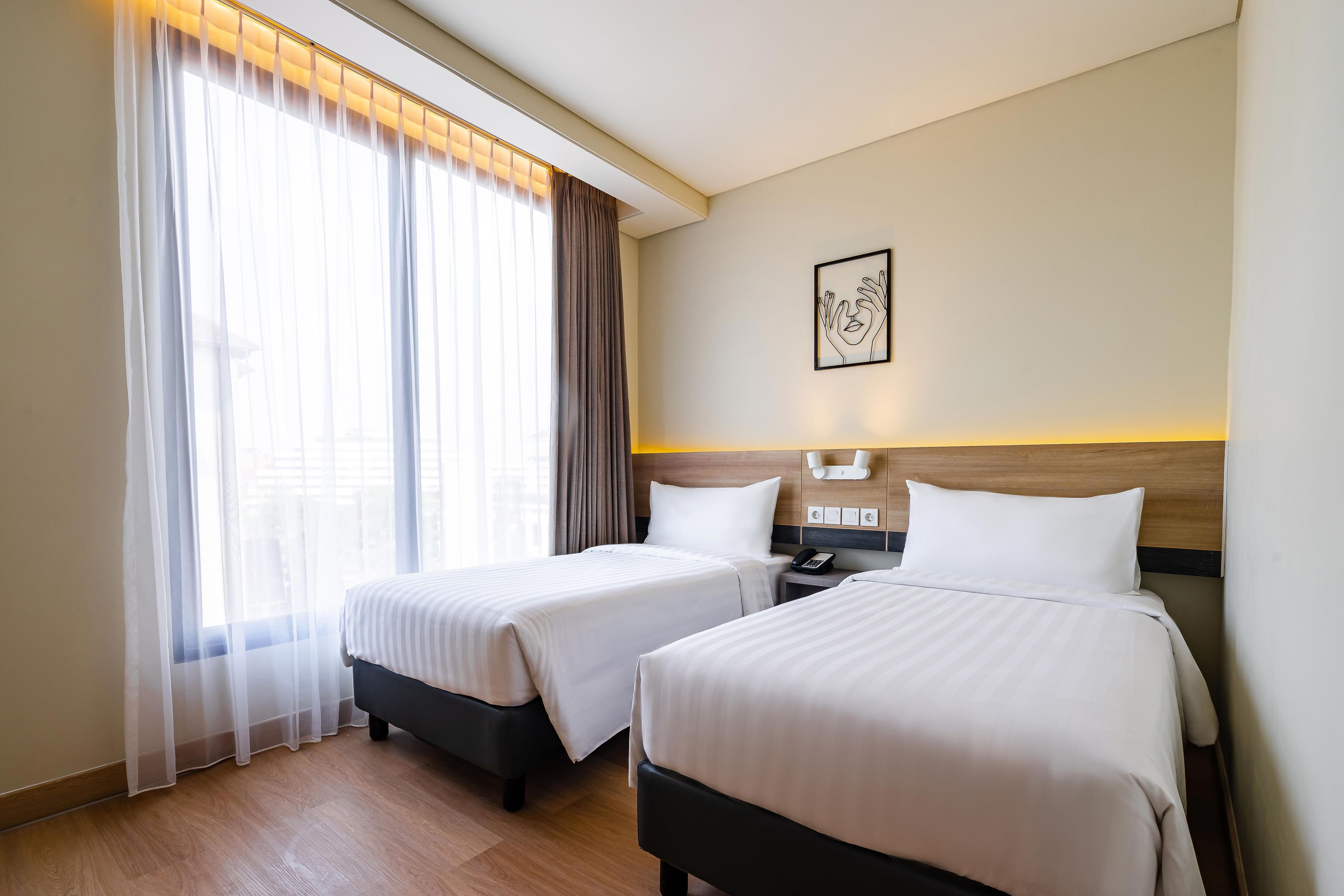 Una habitación de hotel con dos camas, una mesita de noche con teléfono y una lámpara de pared.
