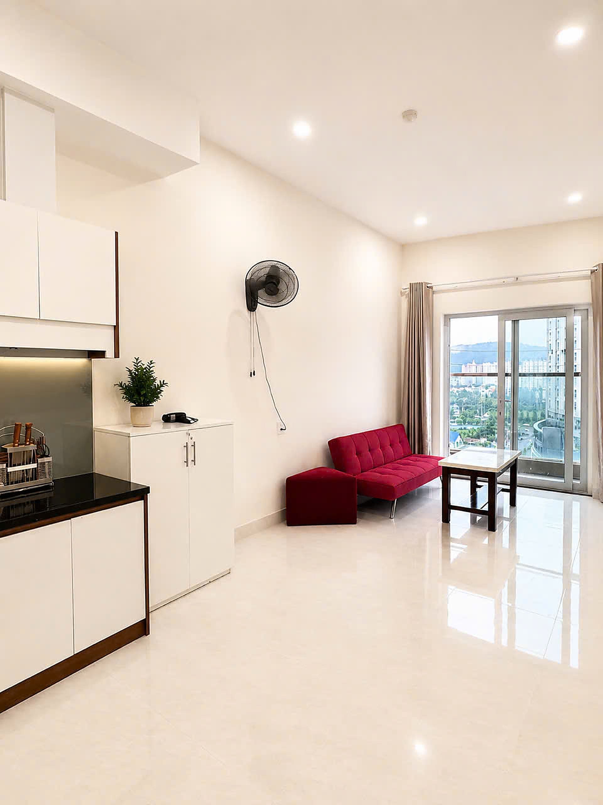Una sala de estar moderna con un sofá rojo, una mesita y una zona de cocina con armarios y una encimera.