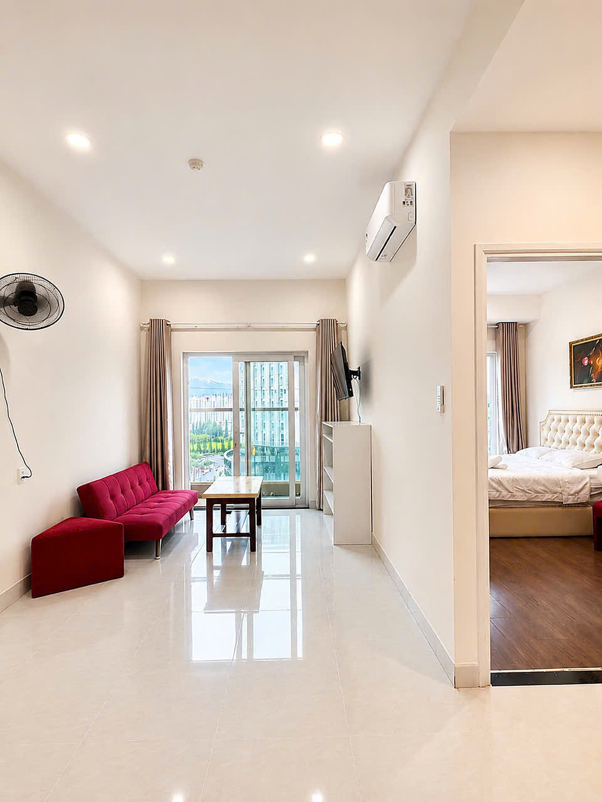 Una habitación de hotel moderna con una cama grande, un área de descanso con un sofá rojo y una mesa, y vistas a través del ventanal.