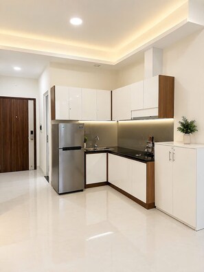 A modern kitchen with white cabinetry, a stainless steel refrigerator, and a black countertop. - Mermaid Seaview-Apartment near beach (Vũng Tàu)