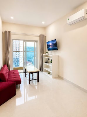 A modern living room with a flat-screen TV, a dining table, red sofas, and a city view through large windows. - Mermaid Seaview-Apartment near beach (Vũng Tàu)