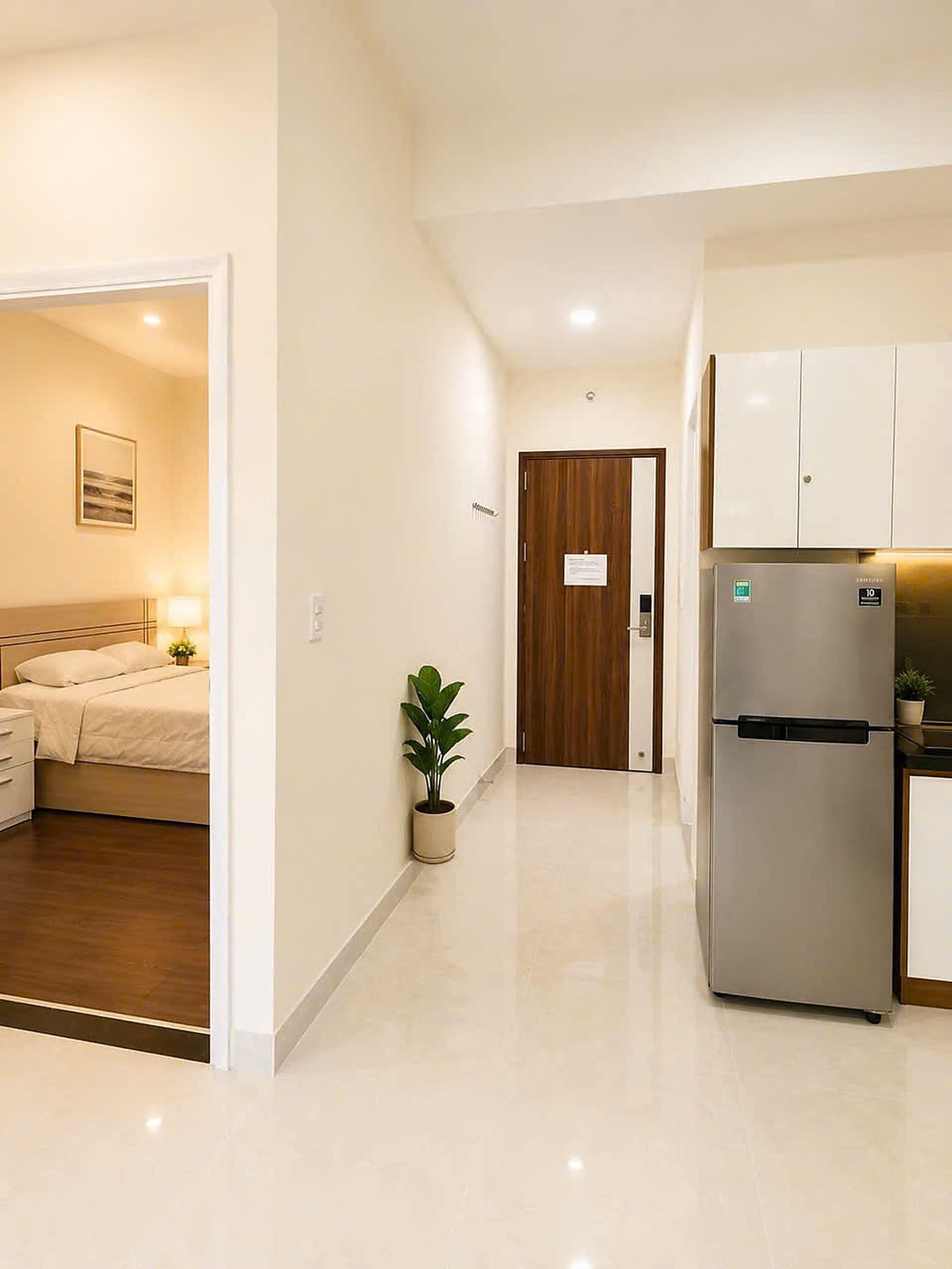 Una habitación de hotel con cama, mesita de noche, lámpara y una planta en maceta.