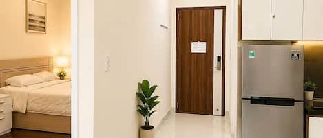 A hotel room with a bed, bedside table, lamp, and a potted plant.