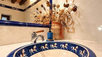A bathroom with a blue ceramic sink, a wooden faucet, and a decorative vase with dried plants.