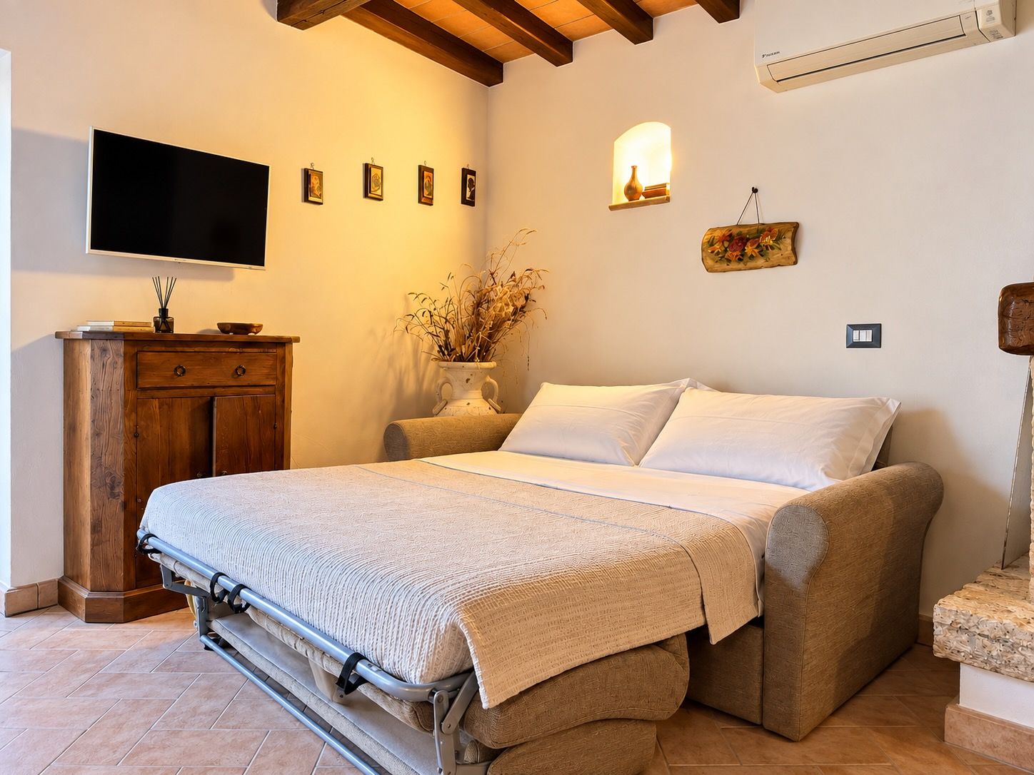Una camera da letto con un letto, una TV, una cassettiera in legno e un condizionatore d'aria a parete.