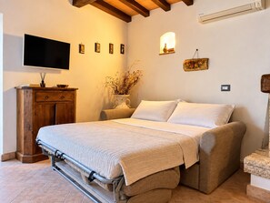A bedroom with a bed, a TV, a wooden dresser, and a wall-mounted air conditioner.