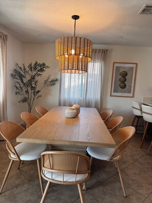 A dining area with a wooden table, wicker chairs, a hanging light fixture, and a plant. -     Resort-Style Desert Oasis + Pool & Spa (Bermuda Dunes)