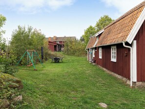 A rural property with a grassy yard, a swing set, and a red wooden house with a tiled roof. - Guttamåla by Interhome (Tving)