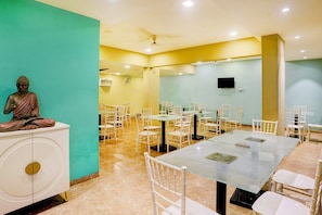 A conference room with a Buddha statue, white chairs, and a flat-screen TV on the wall. - Palette Hotel And Resort Igatpuri (Igatpuri)