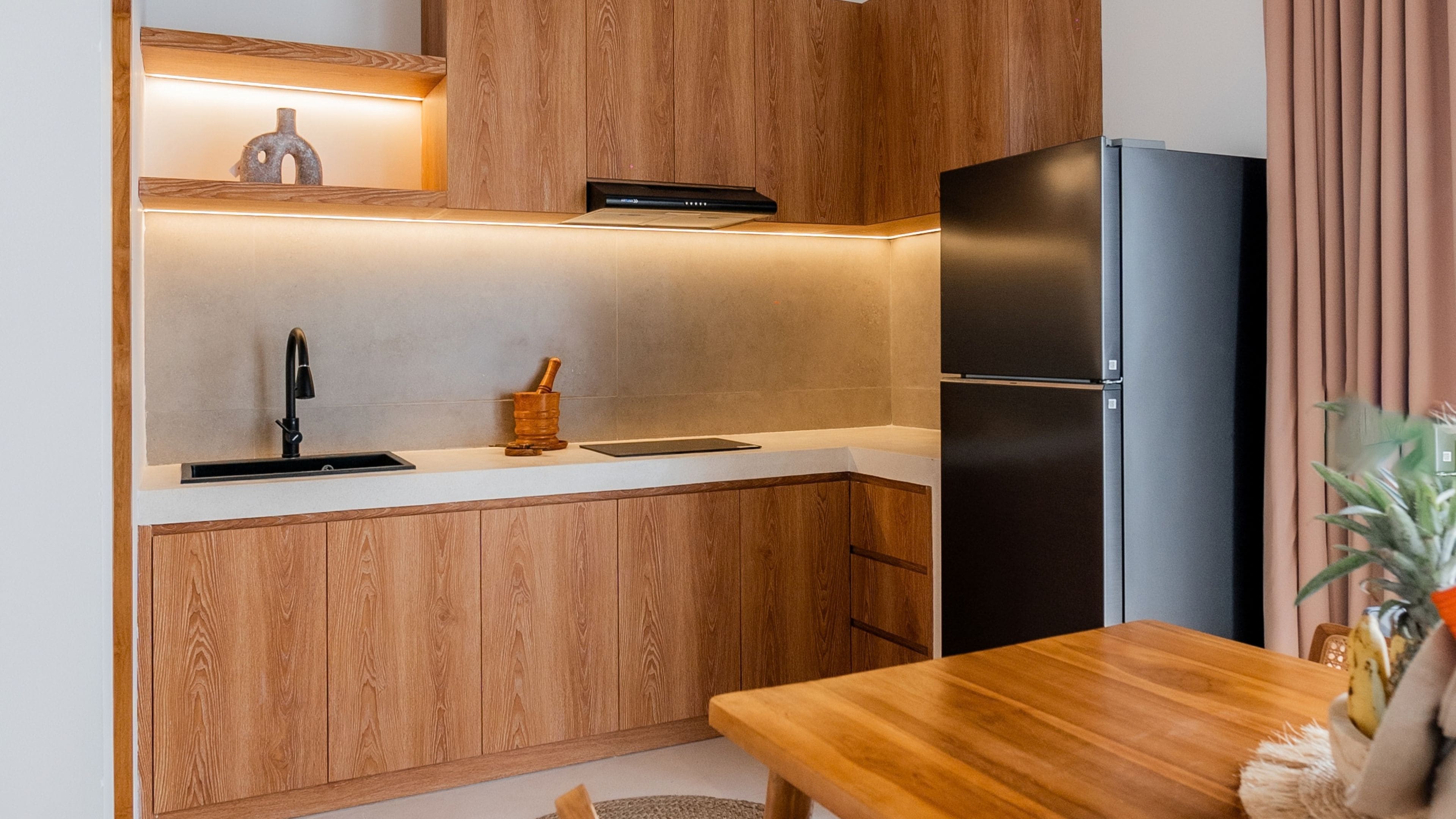 A compact kitchen with wooden cabinets, a black refrigerator, and a wooden dining table.