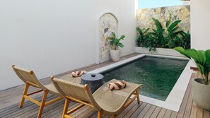 A poolside area with two wicker lounge chairs, a small table, and a stone wall with plants. - Enso Resort (Tabanan)