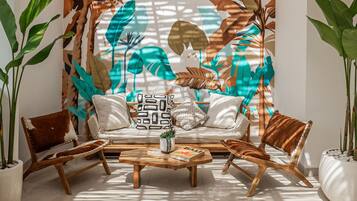 A modern living room with a sofa, two armchairs, a coffee table, and a decorative wall with tropical leaf patterns.