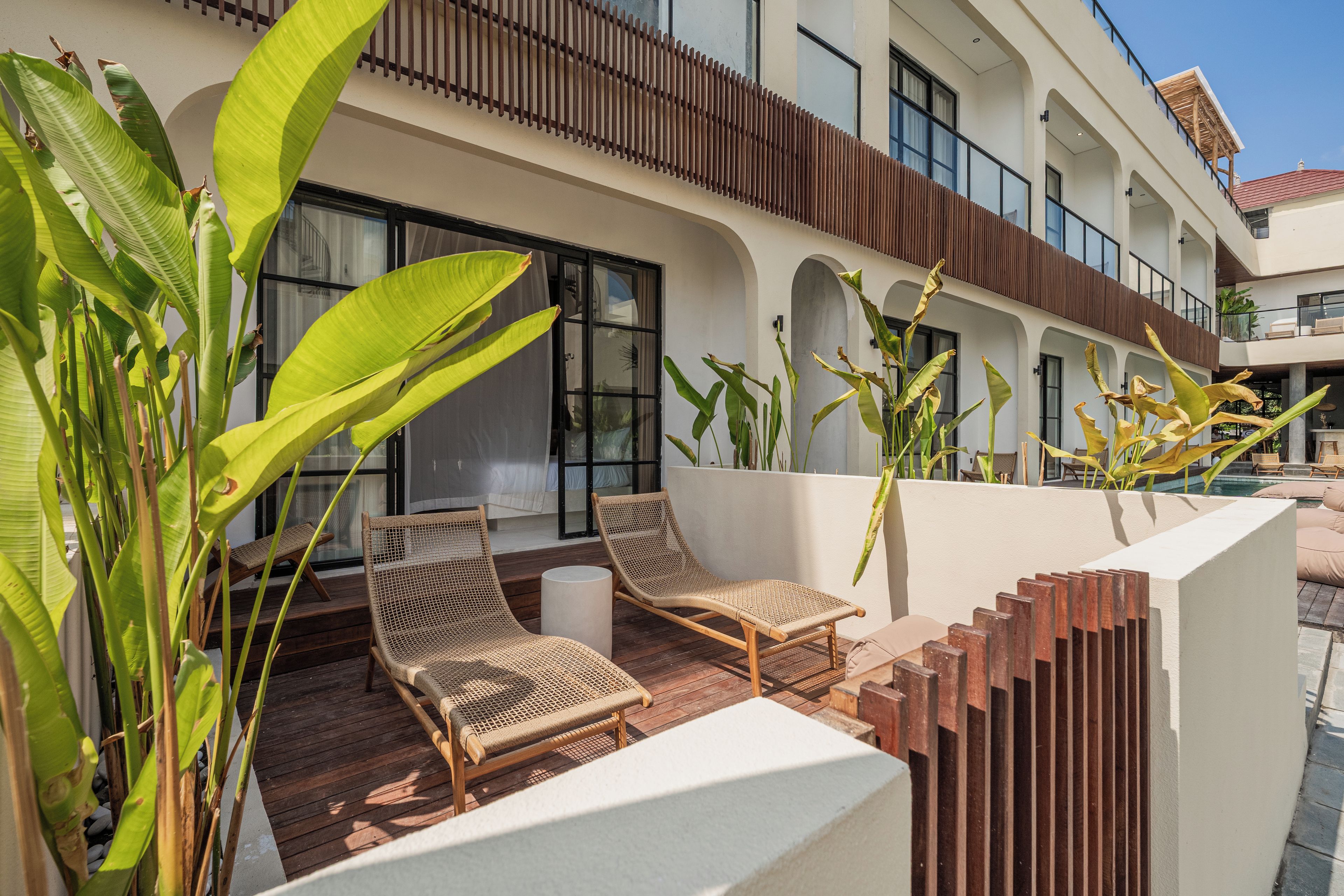 A modern hotel with a pool area featuring wicker chairs and tropical plants.