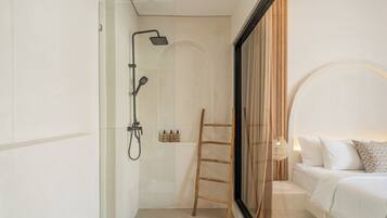 A modern bathroom with a shower, a wooden ladder, and a bed with white bedding.