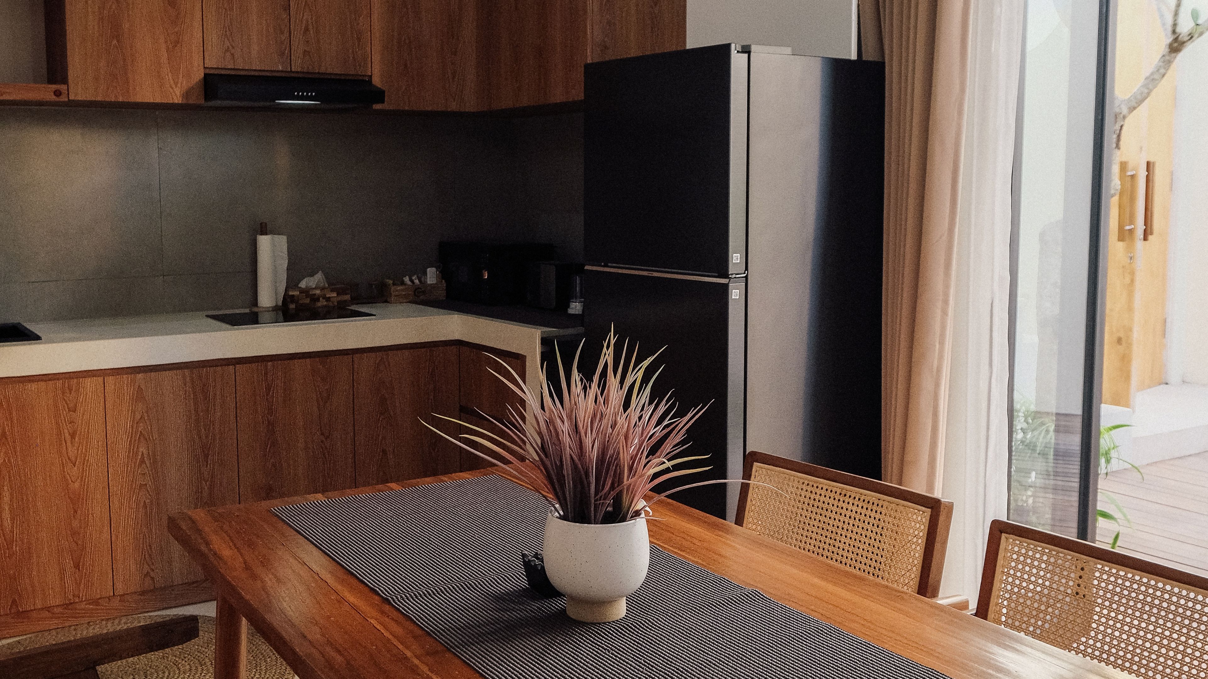 Una cucina moderna con mobili in legno, un frigorifero nero e un tavolo da pranzo con un sottopiattino intrecciato.