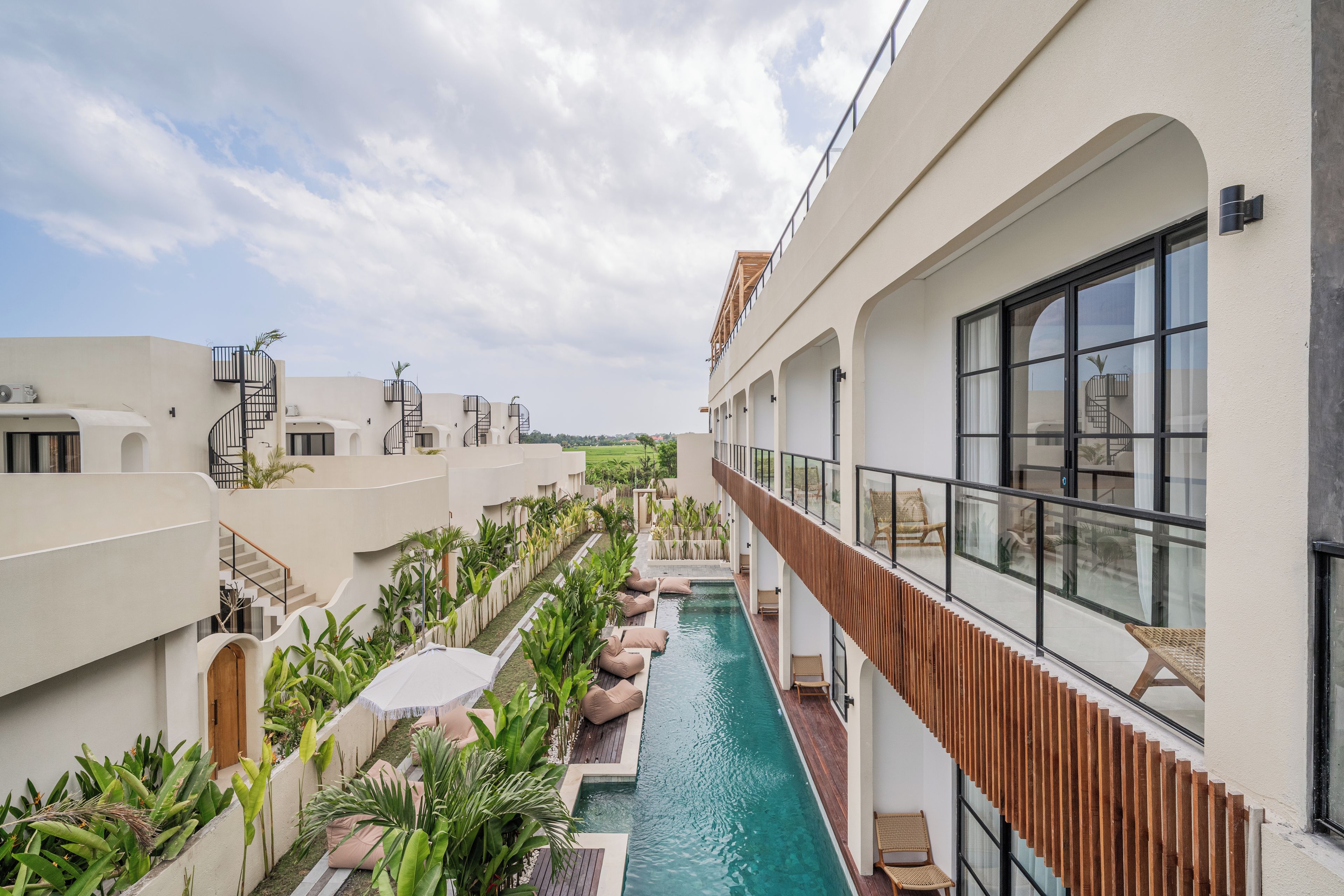 A modern hotel with a central pool, outdoor seating, and a view of the surrounding landscape.