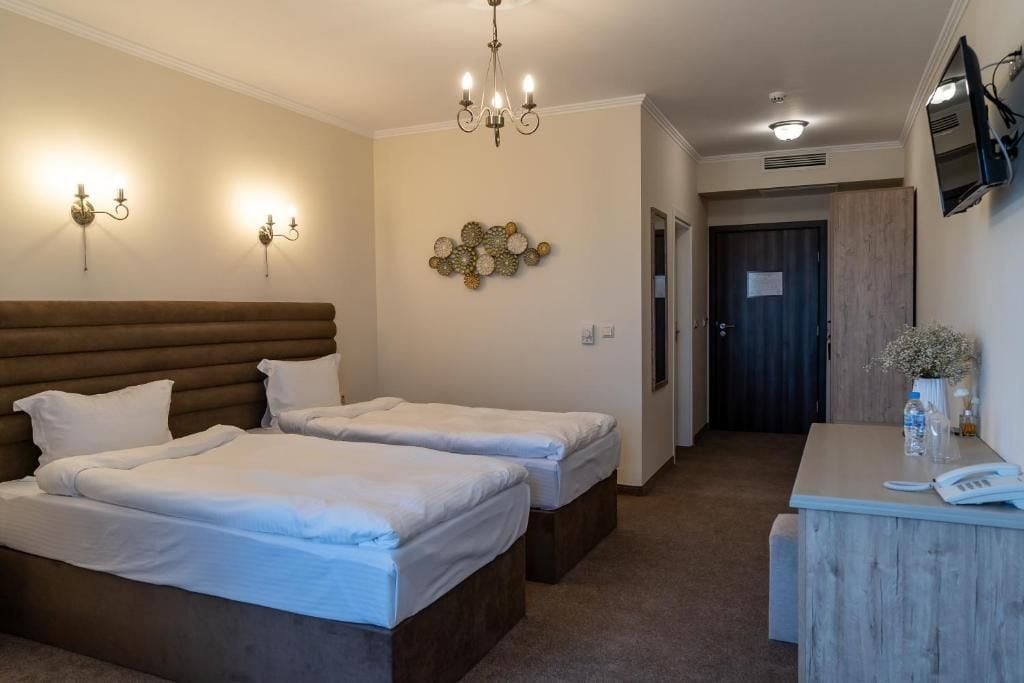 A hotel room with two beds, a desk, a chandelier, wall sconces, and a decorative wall piece.