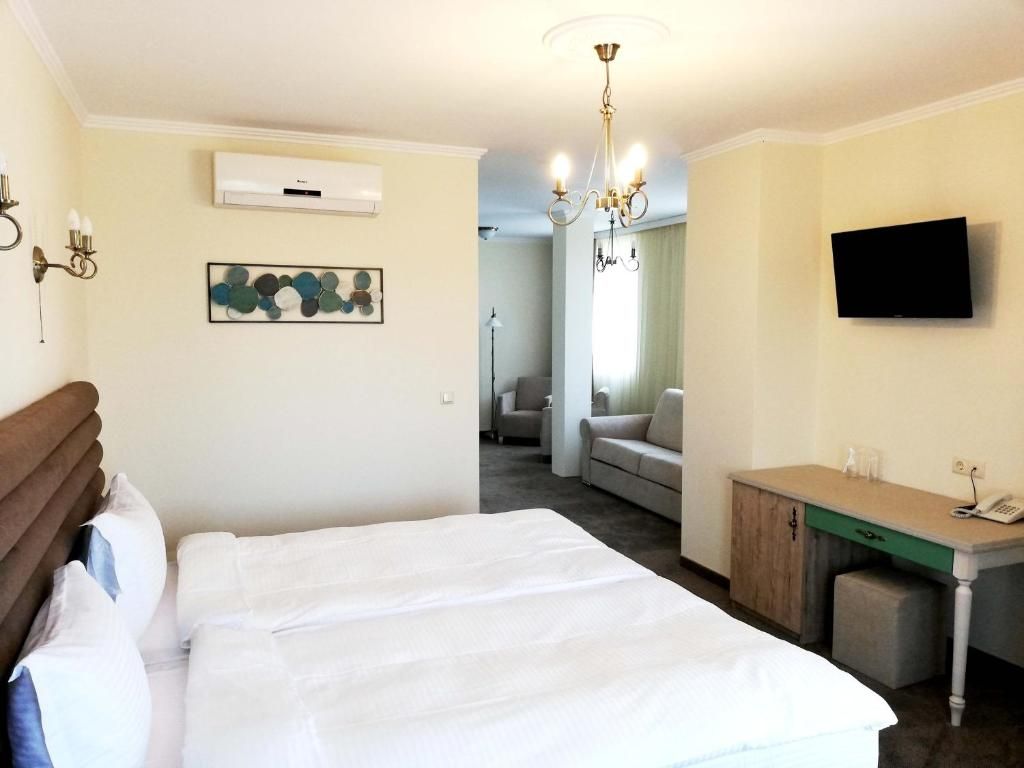 A hotel room with a bed, a desk, a television, an air conditioning unit, a chandelier, and a painting on the wall.