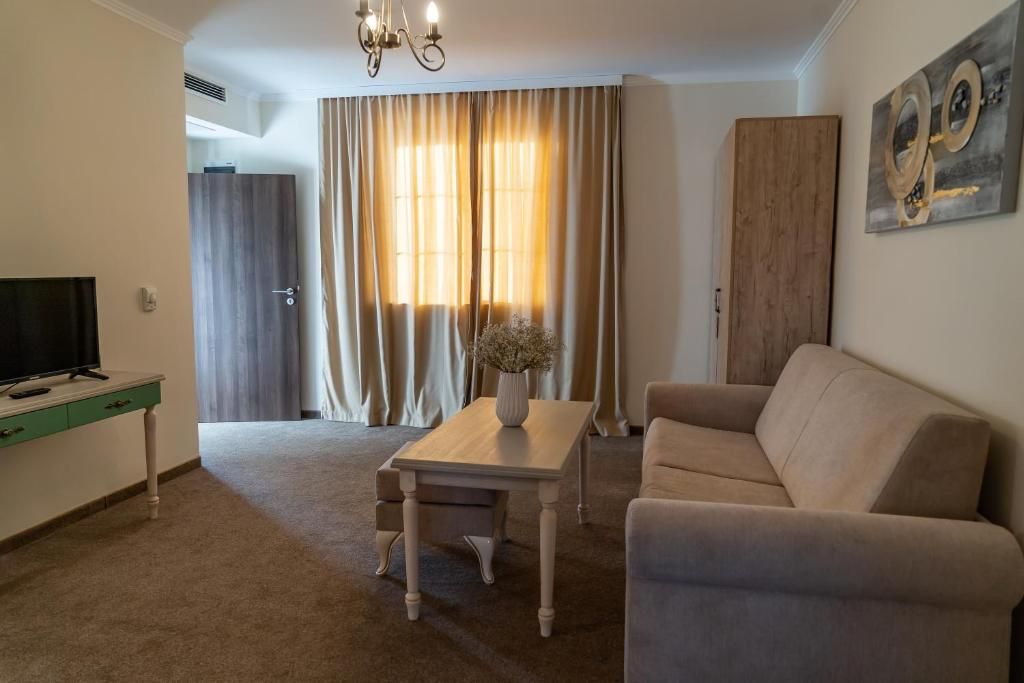 A living room with a sofa, a coffee table, a TV, and a window with curtains.
