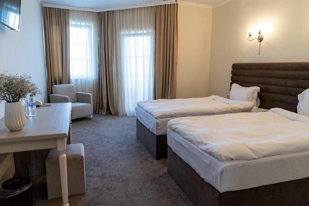 A hotel room with two beds, a desk, a chair, and a window with curtains.