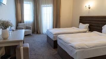 A hotel room with two beds, a desk, a chair, and a window with curtains.