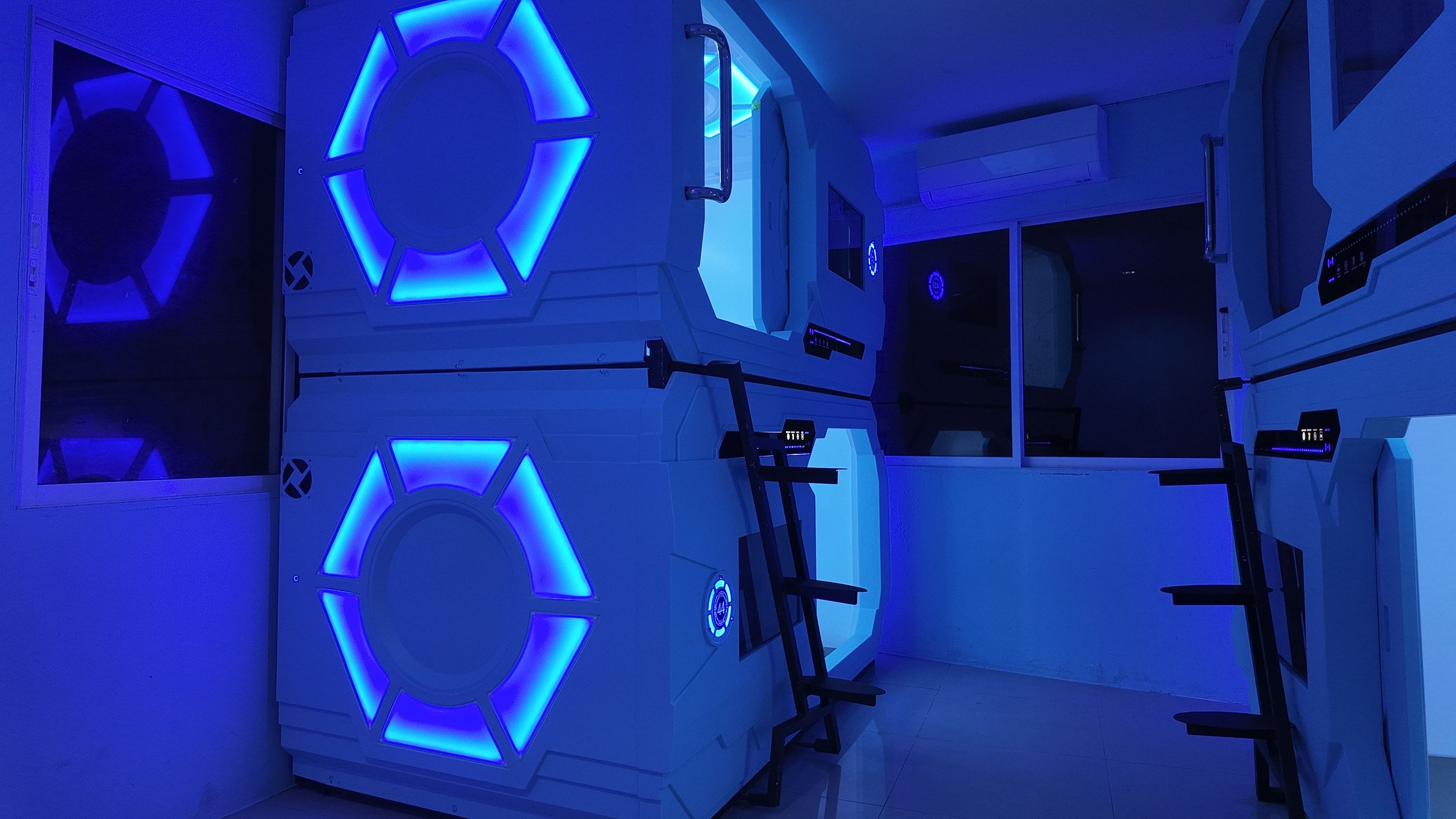 Une pièce dont les murs sont ornés d’un motif circulaire illuminé de lumière bleue, avec un panneau de contrôle et une fenêtre.