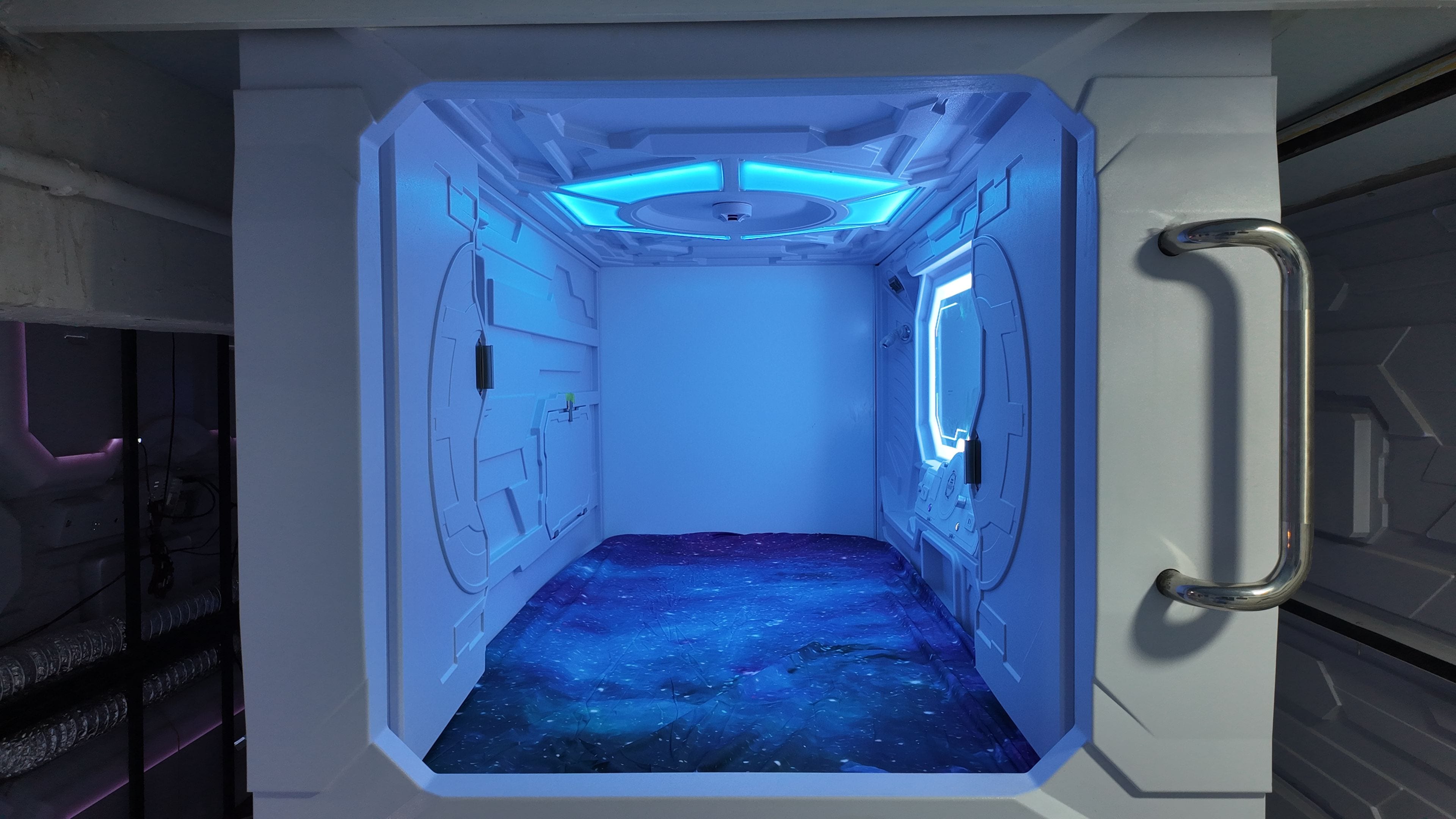 A room with a metallic door handle, a control panel, and a starry space-themed floor.